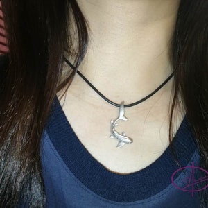 May include: A silver shark pendant necklace on a black cord. The pendant is detailed and realistic.