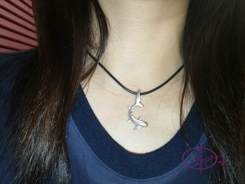 May include: A silver shark pendant necklace on a black cord. The pendant is detailed and realistic.