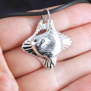 May include: Silver-toned pendant necklace featuring a detailed, three-dimensional design of a mola mola fish. The pendant is attached to a black rubber cord.