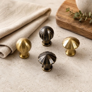 May include: Four round cabinet knobs with a faceted, ribbed surface design. Two knobs feature a bright brass finish, while the other two knobs have a darker, antiqued bronze finish. Each knob has a central stem and a circular base for mounting.