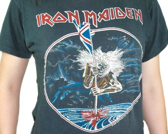 May include: A dark gray t-shirt with a circular graphic of a skeleton holding a flag that says "Iron Maiden".