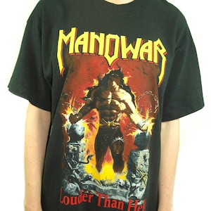 May include: Black t-shirt with a graphic print of a muscular man with long hair and a beard, standing in front of a fiery background. The text "MANOWAR" is printed in yellow and red letters above the image, and the text "Louder Than Hell" is printed in red letters below the image.