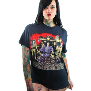 May include: A black t-shirt with a graphic print of Ozzy Osbourne and the band Black Sabbath. The shirt features a red, yellow, and black color scheme. The text "Ozzy Osbourne" is printed in gold lettering.