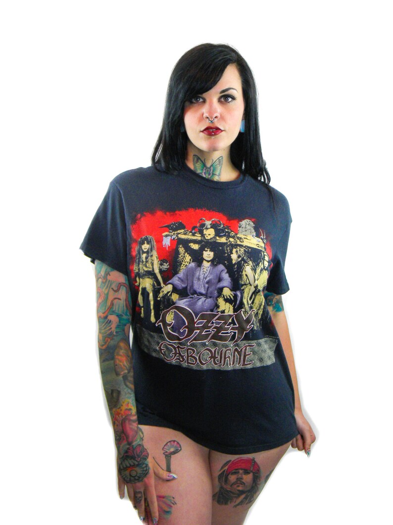 May include: A black t-shirt with a graphic print of Ozzy Osbourne and the band Black Sabbath. The shirt features a red, yellow, and black color scheme. The text "Ozzy Osbourne" is printed in gold lettering.