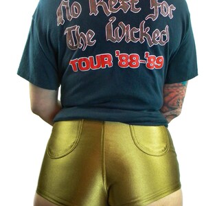 May include: A black t-shirt with the text "No Rest For The Wicked Tour '88-'89" printed on the back. The person is wearing gold shorts.