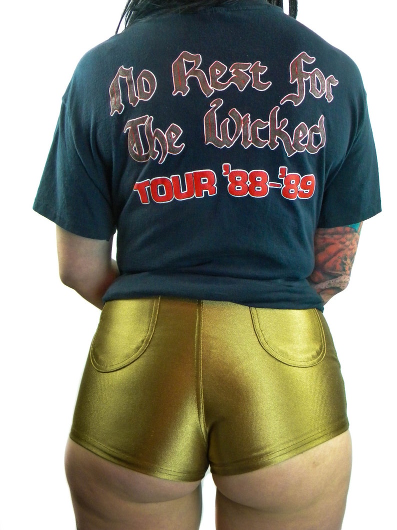 May include: A black t-shirt with the text "No Rest For The Wicked Tour '88-'89" printed on the back. The person is wearing gold shorts.