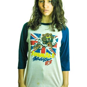 May include: A white and blue baseball tee shirt with a graphic of a tiger and the text "ANIMALS World Tour 83".