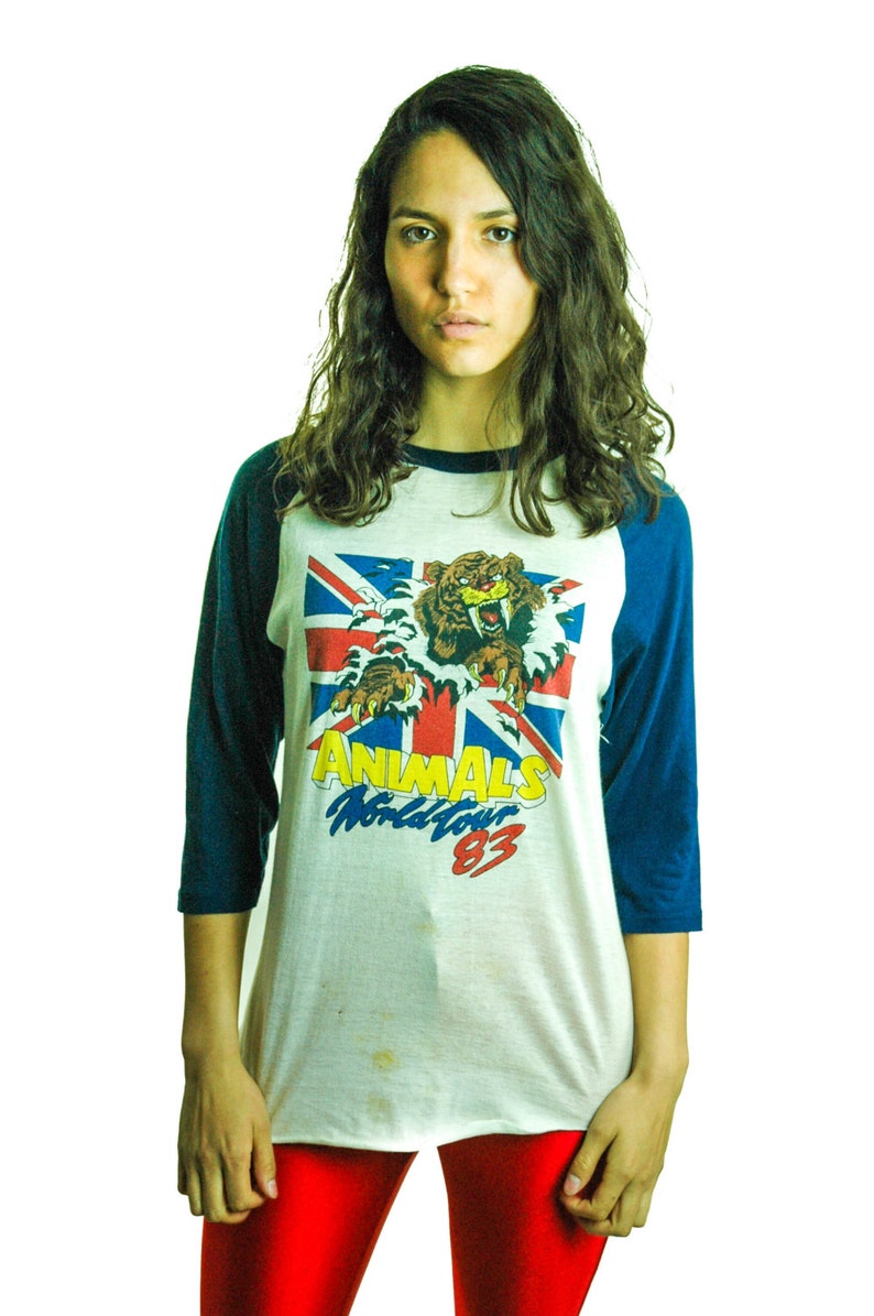 May include: A white and blue baseball tee shirt with a graphic of a tiger and the text "ANIMALS World Tour 83".
