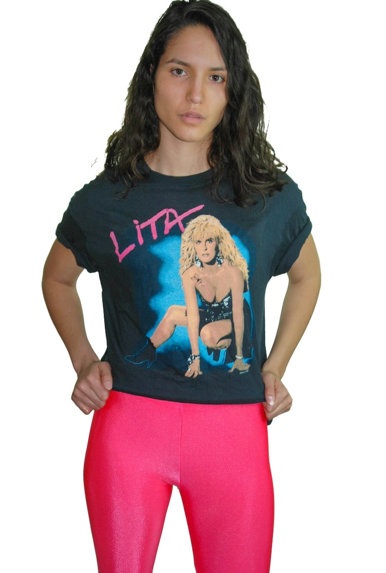 Puede incluir: Una camiseta negra con un estampado gr&aacute;fico de una mujer con cabello rubio. El texto "Lita" est&aacute; impreso en rosa en la camiseta.