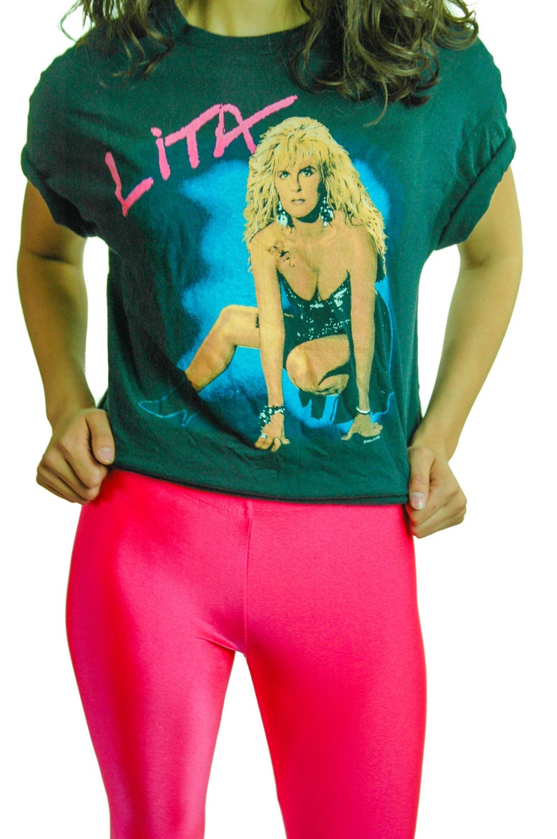 Puede incluir: Una camiseta negra con un estampado gr&aacute;fico de una mujer con cabello rubio. El texto "LITA" est&aacute; impreso en la camiseta en rosa.