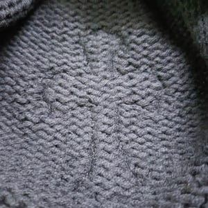 Puede incluir: Primer plano de una tela de punto gris oscuro con un patr&oacute;n texturizado y tejido. La tela parece gruesa y c&aacute;lida, con puntadas visibles que crean un efecto de nervaduras diagonales. El material es probablemente lana o una fibra similar.