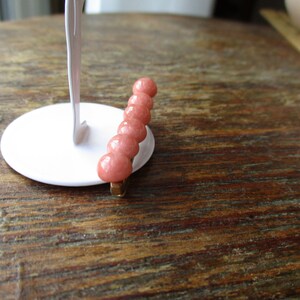 May include: A pink stone hair clip with six round beads. The clip is made of metal and has a gold finish.