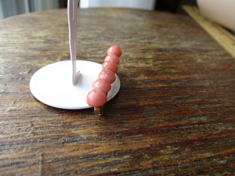 May include: A pink stone hair clip with six round beads. The clip is made of metal and has a gold finish.