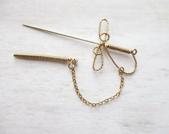 May include: A gold-toned brooch with a delicate butterfly design. The brooch features a coiled wire pin and a chain attached to the bottom.