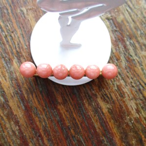 May include: A gold bar with six round, pink beads. The beads are evenly spaced on the bar.