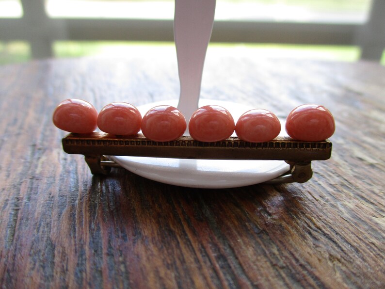 May include: A gold-toned bar brooch with six pink oval-shaped stones.