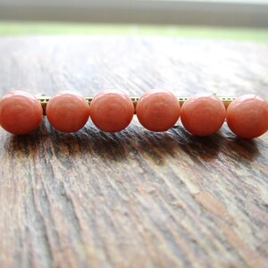 May include: A row of six coral-colored beads strung on a gold wire.