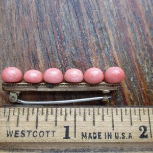 May include: A row of six pink cabochon stones set on a gold-toned bar with a silver-toned clasp. The bar is about 1 inch long.