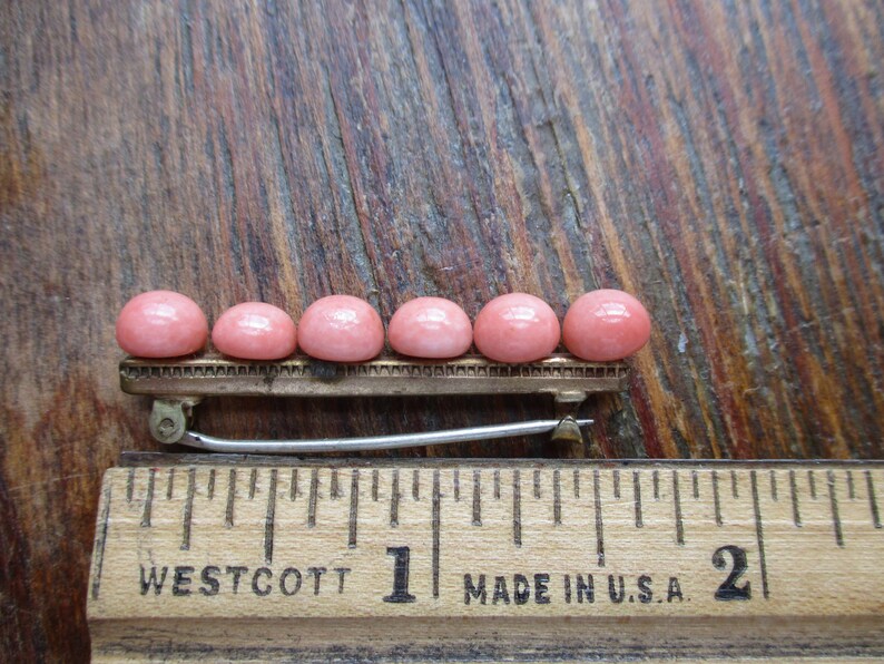 May include: A row of six pink cabochon stones set on a gold-toned bar with a silver-toned clasp. The bar is about 1 inch long.