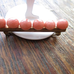 May include: A vintage brooch with six round, light pink stones set in a gold-toned metal base.