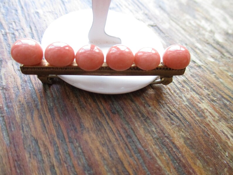 May include: A vintage brooch with six round, light pink stones set in a gold-toned metal base.
