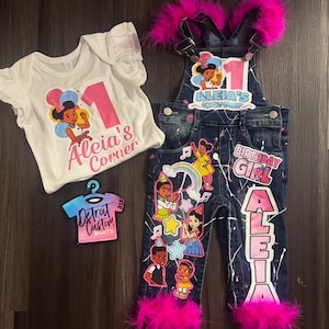 Op de afbeelding: Een witte romper en een spijkerbroek set met een verjaardagsthema. De romper heeft een roze nummer 1 en de tekst "Aleia's Corner". De overall is versierd met kleurrijke graphics, roze accenten en de naam "Aleia".