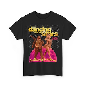 May include: A black t-shirt featuring a graphic of two dancers, Guillermo and Witney, with the text Dancing with the Stars 2026. The design includes a gold glittery logo, a pink moon-like background, and a black dotted pattern above the dancers.