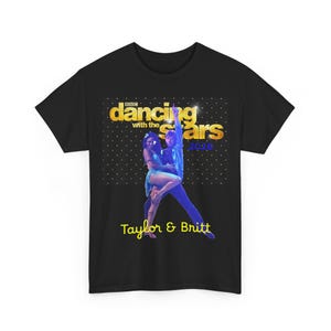 May include: A black short-sleeved t-shirt featuring a graphic of two dancers. The text reads BBC dancing with the stars 2026 and Taylor & Britt. The background of the graphic is black with white dots and gold lettering for the show title.