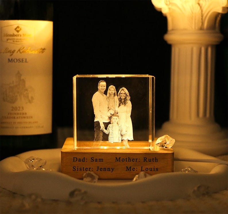 May include: A clear rectangular glass block featuring a laser-etched family portrait, illuminated from below by a wooden base. The base is engraved with the text: Dad: Sam, Mother: Ruth, Sister: Jenny, Me: Louis, creating a personalized display piece.