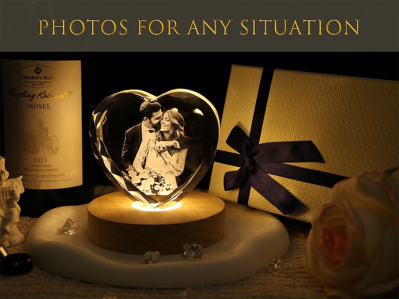 May include: A heart-shaped glass block featuring a laser-etched photograph of a couple, illuminated by a round wooden light base. The text "PHOTOS FOR ANY SITUATION" appears at the top. A gift box with a dark blue ribbon sits to the right.