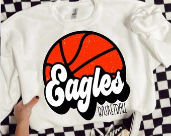 Könnte beinhalten: Weißer Pullover mit einem roten und schwarzen Basketball-Motiv und dem Text "Eagles Basketball".