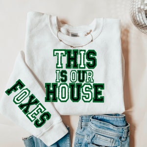 May include: White sweatshirt with green and black text that reads "This is our house" and a green and black sleeve with the word "Foxes".