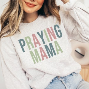 May include: A gray sweatshirt with the text "Praying Mama" in colorful letters. The letters are in shades of green, pink, and blue.