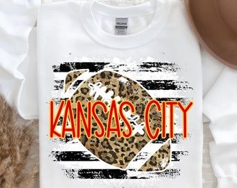 May include: White sweatshirt with a black and white striped design featuring a leopard print football with the text "KANSAS CITY" in red.