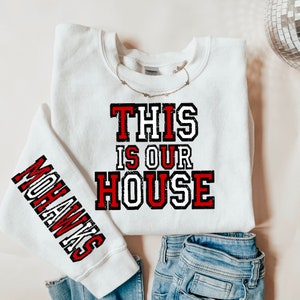 May include: White sweatshirt with red and black text that reads "This is our house" and a red and black sleeve graphic that reads "Mohawks".