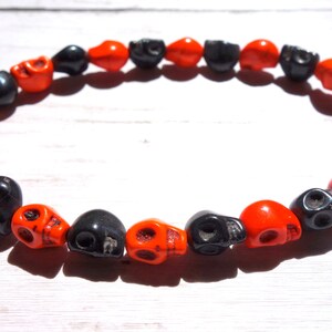 May include: A black and orange skull bead necklace. The beads are alternating colors and are shaped like skulls.