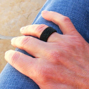 May include: A black woven ring on a person's finger.