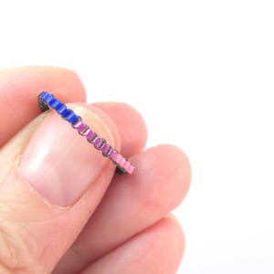 Könnte beinhalten: Ein dünner Ring mit einem Farbverlauf aus rosa und blauen Emaille-Quadraten.