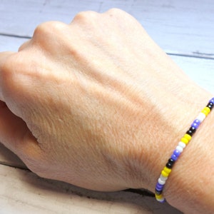 Pode incluir: Um bracelete de contas com contas pretas, brancas, amarelas e roxas alternadas.