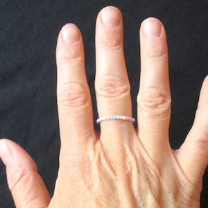 Puede incluir: Una mano con un fino anillo de cuentas con cuentas rosas, azules y blancas.