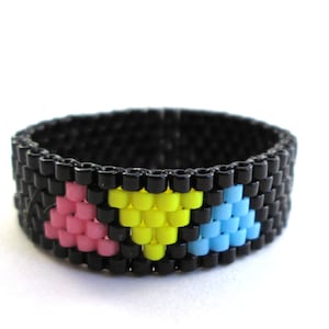 以下が含まれることがあります： 黒ビーズのリングに、ピンク、黄色、青のハート型のデザインが3つ施されています