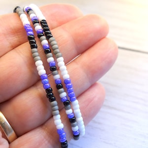 May include: Three strands of beaded jewelry in purple, gray, white, and black colors.