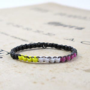 以下が含まれることがあります： 黒色のチェーンブレスレットに、黄色、白、ピンクのビーズのバンドが付いている