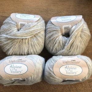 Puede incluir: Cuatro madejas de hilo gris claro, etiquetadas como "Alpine Valley" y "Lighthouse". El hilo es un material suave y texturizado, ideal para proyectos de tejido o ganchillo. Las etiquetas son blancas con detalles azules.