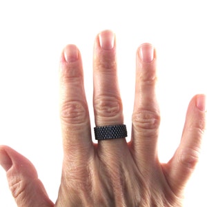 May include: A black beaded ring worn on the ring finger of a hand.