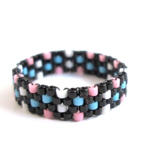 May include: A beaded ring with a pattern of black, white, light blue, and pink beads.