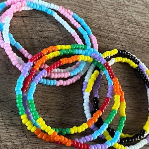 Può includere: Un set di braccialetti colorati con perline, tra cui un braccialetto arcobaleno, un braccialetto bianco e nero e un braccialetto azzurro, rosa e bianco.