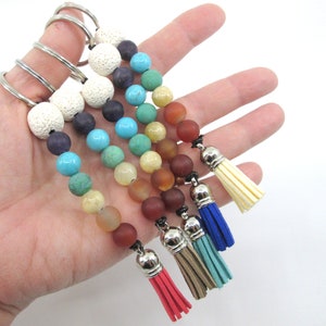 Puede incluir: Un conjunto de cinco llaveros de cuentas de colores con borlas. Cada llavero presenta una combinación de colores diferente de cuentas, incluyendo blanco, azul, verde, amarillo, naranja y rojo. Los llaveros están unidos a llaveros de plata.