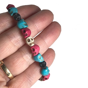 May include: A bracelet made of colorful skull beads. The beads are turquoise, pink, white, and black. The bracelet is strung on elastic.