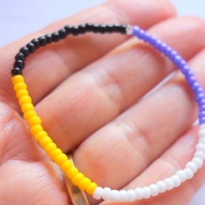 以下が含まれることがあります： 黒、黄、白、紫のビーズで作られたブレスレットです。